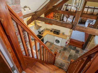 A kitchen with wooden countertops appliances and tiled flooring viewed from wooden stairs at Oak Cottage in North Molton