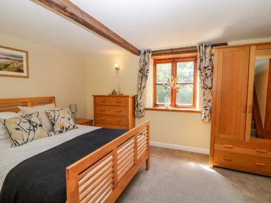 A bedroom with a wooden bed frame chest of drawers and wardrobe by a window at Oak Cottage in North Molton