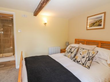 A bedroom with a wooden bed and floral cushions and an en suite bathroom at Oak Cottage in North Molton