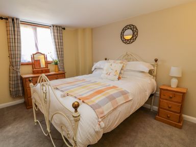 A bedroom with a metal bed frame wooden dressers a bedside table with a lamp and plaid curtains at Oak Cottage in North Molton
