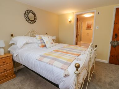 A bedroom with a white bed and patterned cushions a wooden nightstand and a door leading to a bathroom at Oak Cottage in North Molton