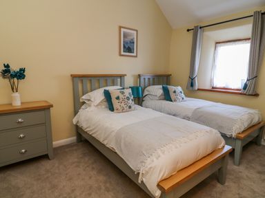 A bedroom with two single beds side by side a window with curtains and a chest of drawers with flowers at Oak Cottage in North Molton