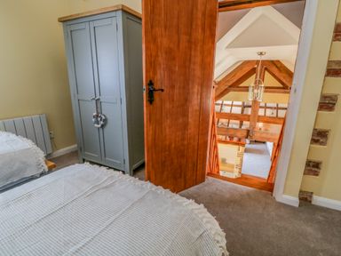 A bedroom with a bed and wardrobe and a wooden door open to a staircase with beams at Oak Cottage in North Molton