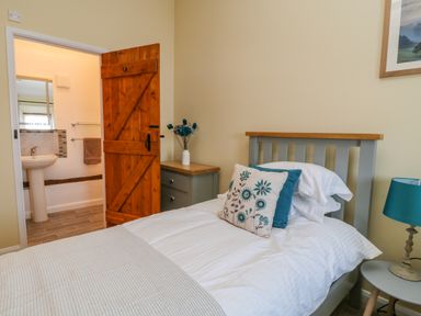A bedroom with a single bed beside a nightstand a wooden door open to a bathroom at Oak Cottage in North Molton