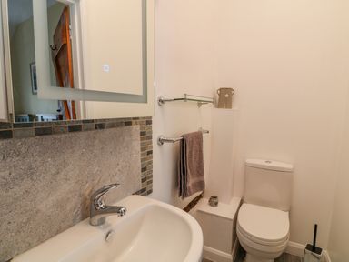 A bathroom with a sink, mirror, towel rack, toilet, and wall shelf at Oak Cottage in North Molton