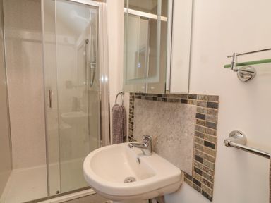 A bathroom with a shower enclosure a white sink with a faucet a hand towel on a ring and a mirror cabinet above the sink at Oak Cottage in North Molton