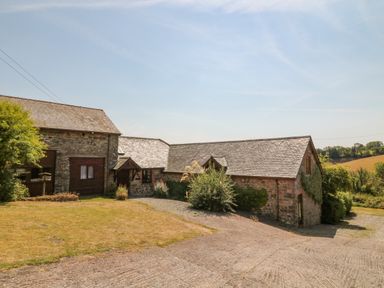 An exterior view of stone buildings with slate roofs surrounded by grass and bushes at Oak Cottage in North Molton