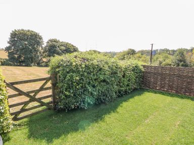 A garden with a wooden gate hedges and a woven fence at Oak Cottage in North Molton