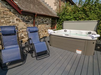 An outdoor area with two blue reclining chairs and a hot tub next to a stone wall at Oak Cottage in North Molton