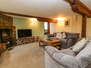 A living room with grey sofas a wooden coffee table a stone fireplace and a television at The Hawthorns in North Molton