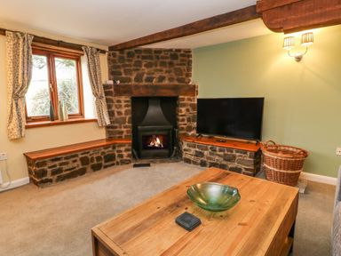 A living room with a stone fireplace wooden coffee table television and wicker basket at The Hawthorns in North Molton