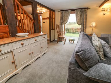A living room with a gray sofa wooden rocking chair sideboard and window with curtains at The Hawthorns in North Molton