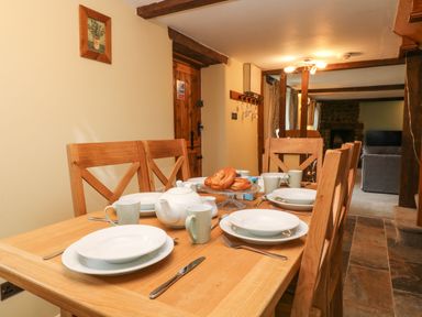 A dining table set with plates cups a teapot and bread with wooden chairs in a room with a wooden door and stone flooring at The Hawthorns in North Molton