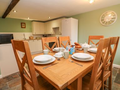 A kitchen with a wooden dining table set with plates cups and cutlery and white cabinets at The Hawthorns in North Molton