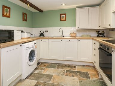 A kitchen with white cabinets wooden countertops a washing machine microwave and oven at The Hawthorns in North Molton