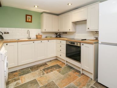A kitchen with white cabinets wooden countertops a stainless steel oven white refrigerator and tiled floor at The Hawthorns in North Molton