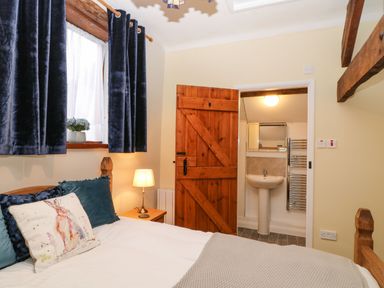 A bedroom with a wooden bed and a door leading to a bathroom with a sink and mirror at The Hawthorns in North Molton