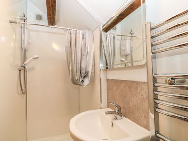 A bathroom with a sink, mirror, shower area with curtain, and a heated towel rail at The Hawthorns in North Molton