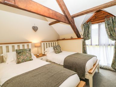 A bedroom with two single beds bedside table lamp and floral curtains at The Hawthorns in North Molton