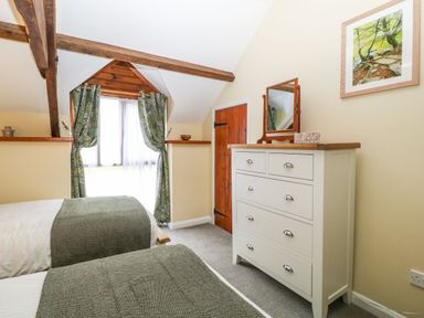 A bedroom with two single beds a white chest of drawers and a window with green curtains at The Hawthorns in North Molton