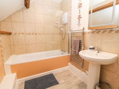 A bathroom with a bathtub shower combination a sink mirror towel rack and a rug at The Hawthorns in North Molton