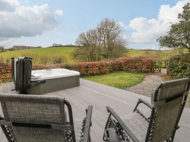 A patio with two chairs and a hot tub overlooking a garden and green hills at The Hawthorns in North Molton