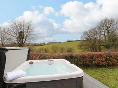 An outdoor hot tub with a white towel on edge overlooking a grassy area and trees at The Hawthorns in North Molton