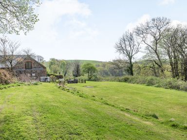 A grassy garden area with trees and a stone building with a patio at The Hawthorns in North Molton