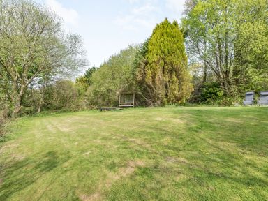A grassy garden area with trees a bench with trellis and two chairs at The Hawthorns in North Molton