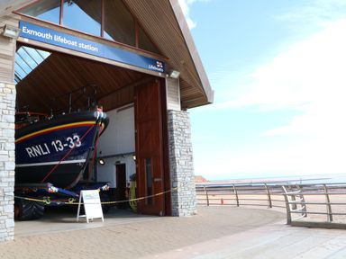 A lifeboat inside the Exmouth lifeboat station near a sandy beach with railings and a blue sky