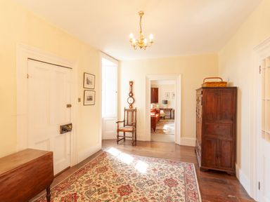 A hallway with a patterned rug wooden chair wooden cabinets and a chandelier at Crablake Farmhouse in Exminster