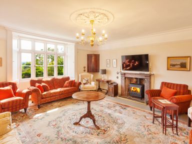A living room with sofas armchairs a round wooden table a fireplace and a large window at Crablake Farmhouse in Exminster