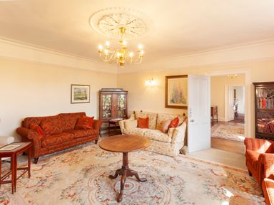 A living room with sofas armchairs wooden cabinet round table and floral carpet at Crablake Farmhouse in Exminster