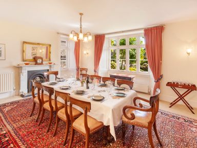A dining room with a set dining table and wooden chairs on a patterned rug at Crablake Farmhouse in Exminster