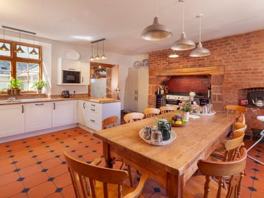 A kitchen with a wooden dining table surrounded by chairs and a brick oven at Crablake Farmhouse in Exminster