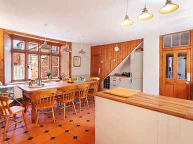 A kitchen dining room with a large wooden table and chairs under three hanging lights next to a large window at Crablake Farmhouse in Exminster
