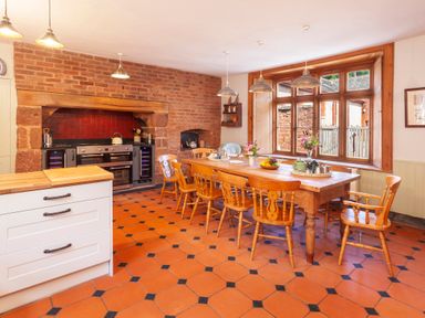 A kitchen with a wooden dining table and chairs a stove set in a brick fireplace and large window at Crablake Farmhouse in Exminster