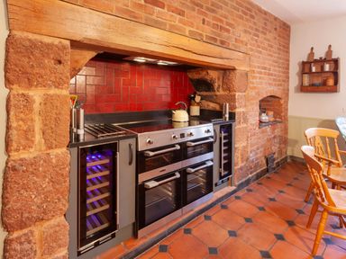 A kitchen area with a stainless steel stove and ovens set into a stone and brick alcove with red tiled backsplash at Crablake Farmhouse in Exminster