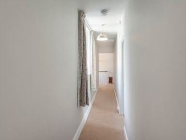 A narrow hallway with windows covered by curtains and beige carpet at Crablake Farmhouse in Exminster