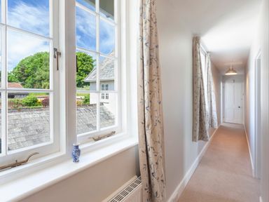 A hallway with floral curtains a white door and a window showing rooftops at Crablake Farmhouse in Exminster