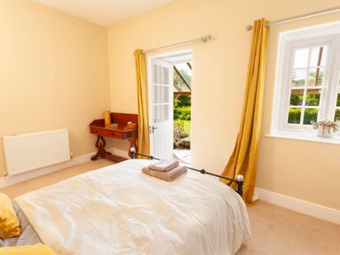 A bedroom with a bed towels on the bed a wooden desk with items on it yellow curtains and a door open to a garden at Crablake Farmhouse in Exminster