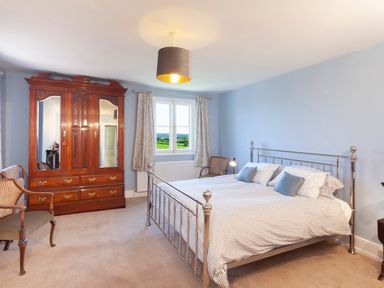 A bedroom with a metal bed frame a wooden wardrobe two chairs and a window with curtains at Crablake Farmhouse in Exminster
