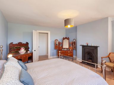 A bedroom with a metal bed frame a fireplace wooden furniture and a chair at Crablake Farmhouse in Exminster