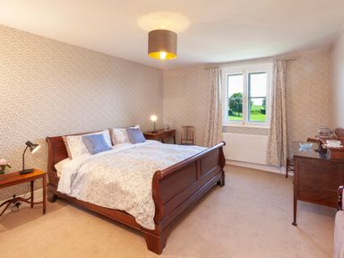 A bedroom with a wooden bed table lamps a window and wallpaper at Crablake Farmhouse in Exminster