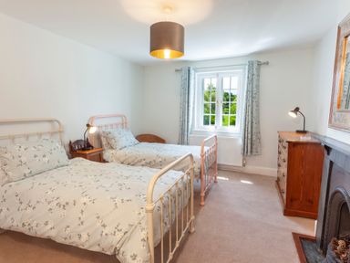 A bedroom with two single beds floral bedding and a window with curtains at Crablake Farmhouse in Exminster