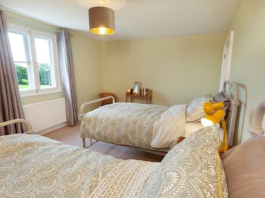 A bedroom with two single beds a window with curtains and a small table with a chair at Crablake Farmhouse in Exminster