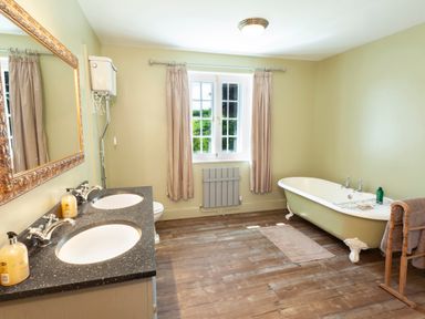 A bathroom with a double sink vanity a freestanding bathtub and a window with curtains at Crablake Farmhouse in Exminster