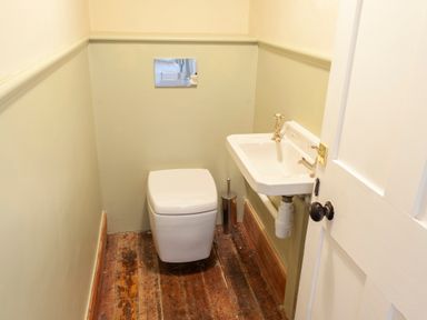 A small bathroom with a toilet and a wall-mounted sink and wooden floor at Crablake Farmhouse in Exminster