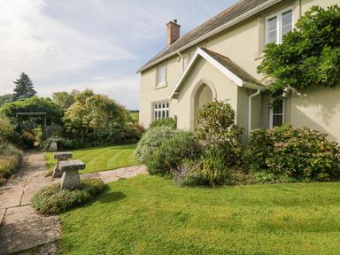 A front garden with a stone path shrubs and a house with a covered entrance at Crablake Farmhouse in Exminster