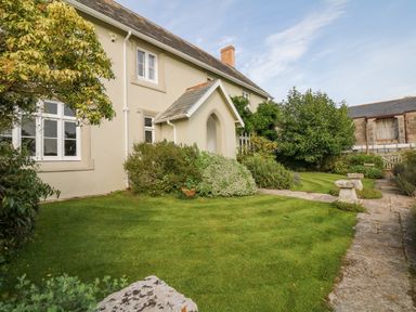 A garden with grass bushes stone benches and a house with white windows at Crablake Farmhouse in Exminster